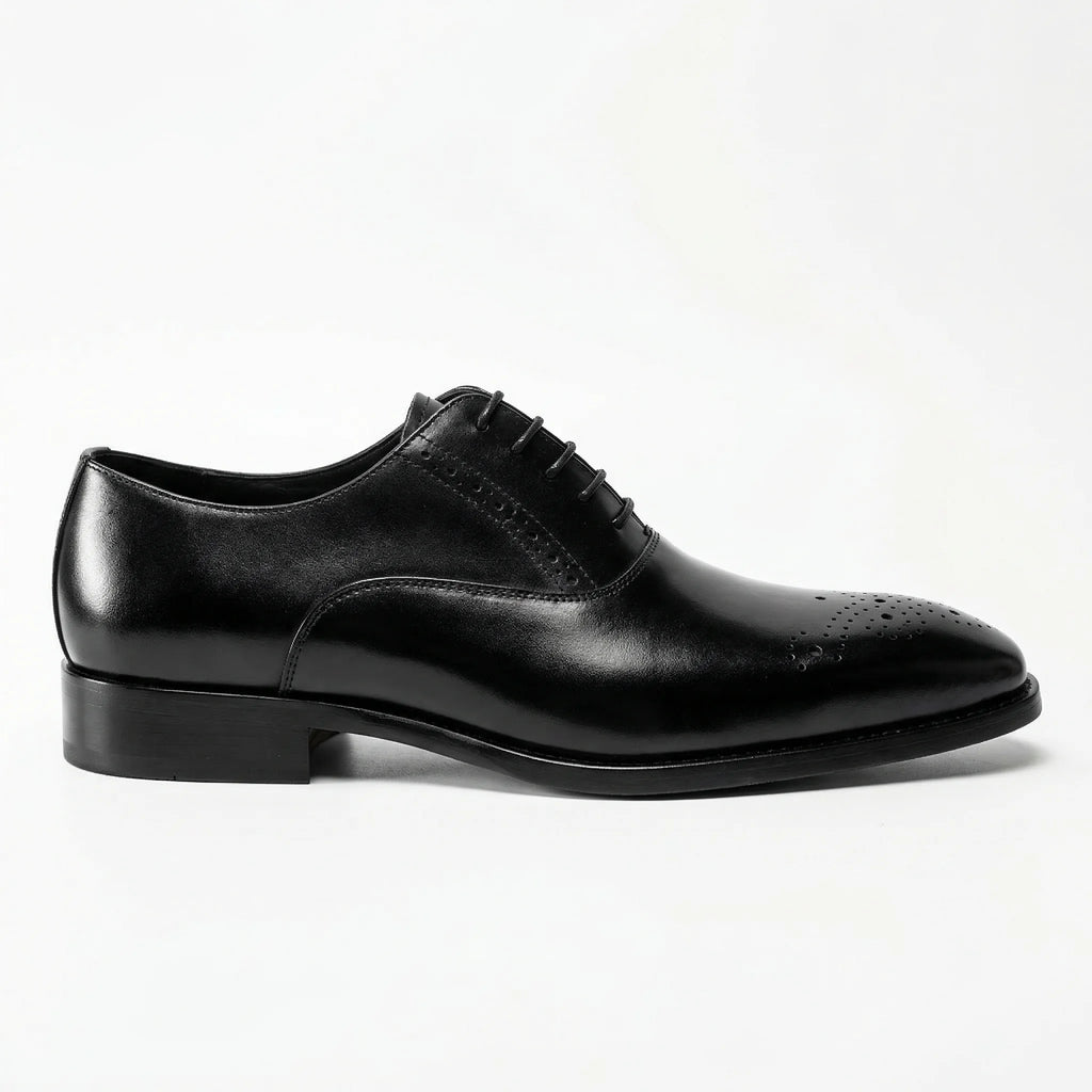 Black leather Oxford dress shoe with brogue detailing on toe, side view, white background.