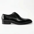 Black leather Oxford dress shoe with brogue detailing on toe, side view, white background.