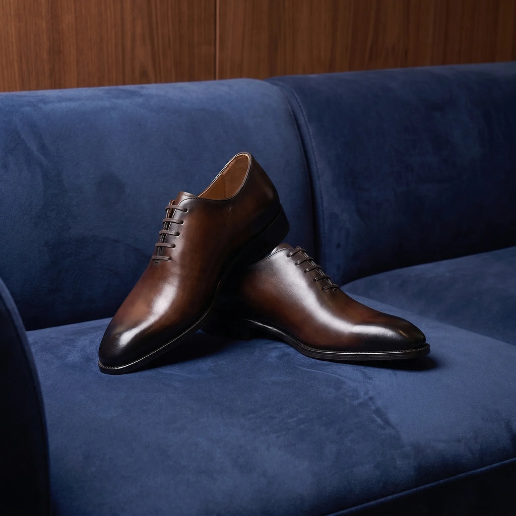 Handmade brogue oxford shoe in full grain leather placed on an elegant and minimalist blue suede sofa
