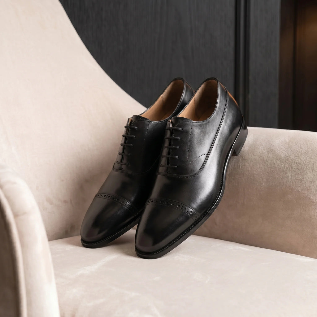 Handmade full-grain leather cap-toe oxford shoe placed on an elegant and minimalist velvet chair
