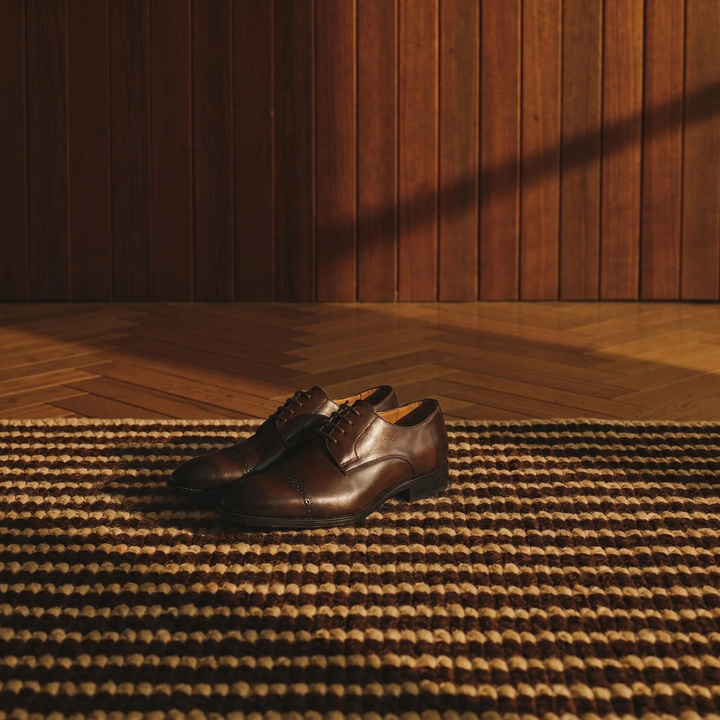 Handcrafted full-grain leather Derby shoe with a reinforced toe, placed on a rug in an elegant, luxurious room