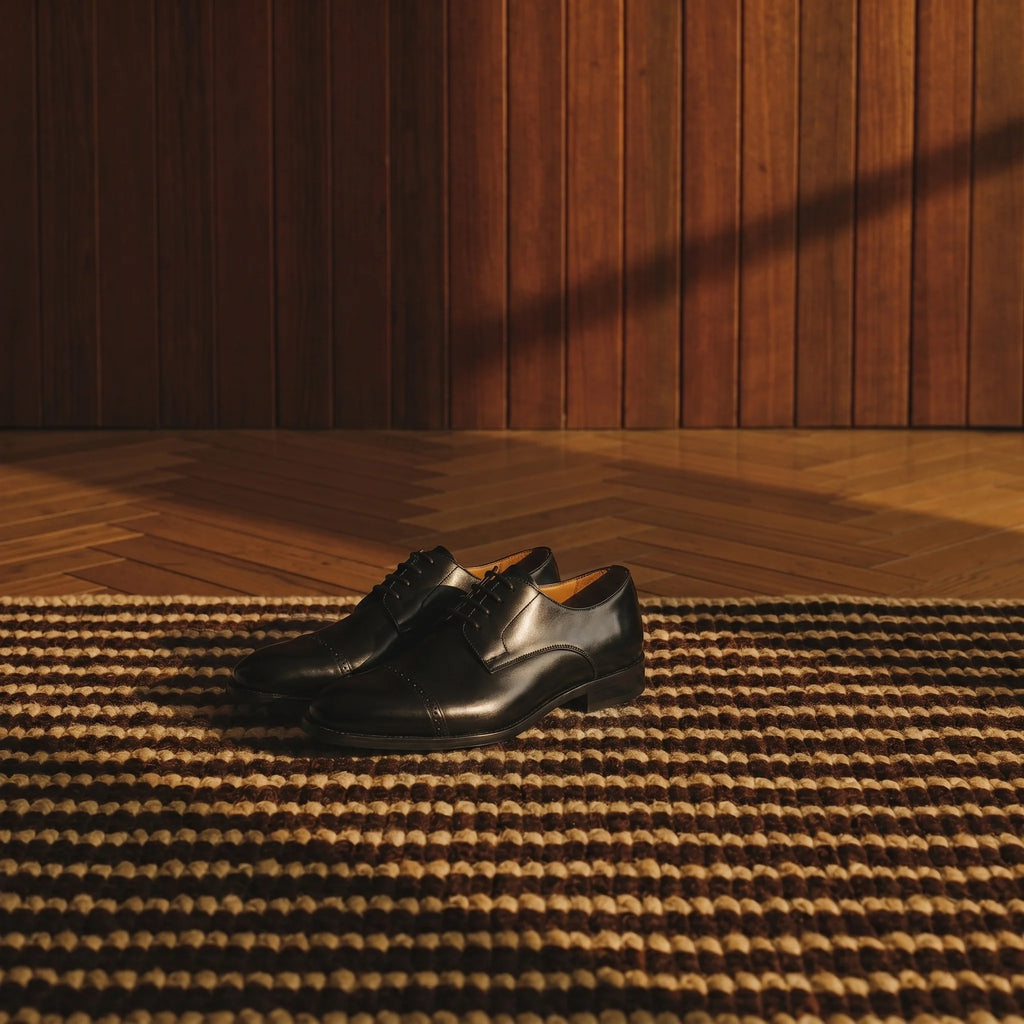 Handcrafted full-grain leather Derby shoe with a reinforced toe, placed on a rug in an elegant, luxurious room