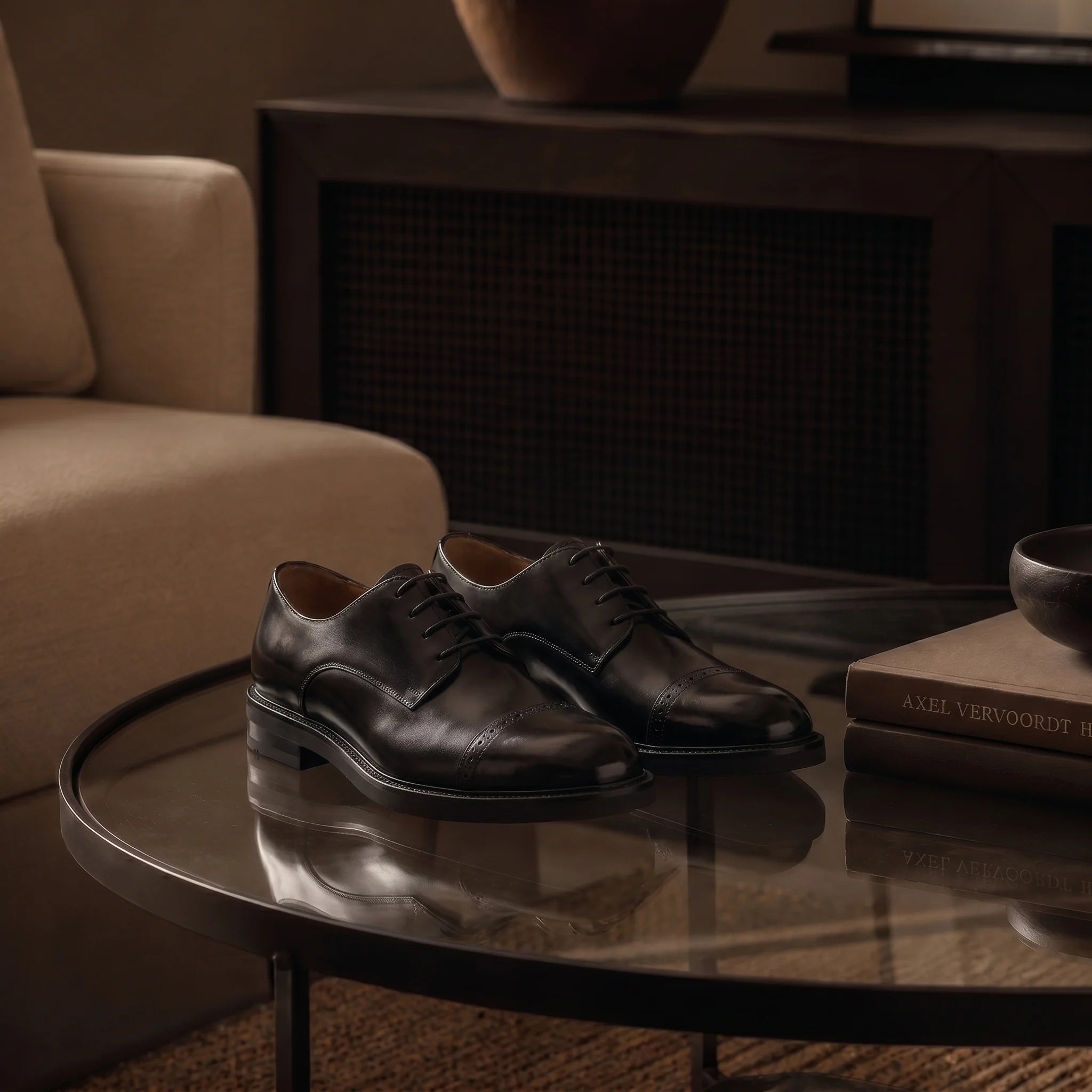 Handmade derby cap-toe shoe in full-grain leather placed on a glass table in a luxurious indoor setting.